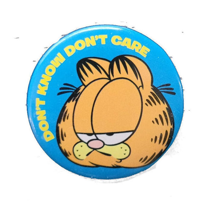 „Runder Button mit Garfield-Motiv und dem englischen Spruch ‚Don’t know. Don’t care.‘ auf weißem Hintergrund. Durchmesser ca. 3,5 cm, Sicherheitsnadel auf der Rückseite.“