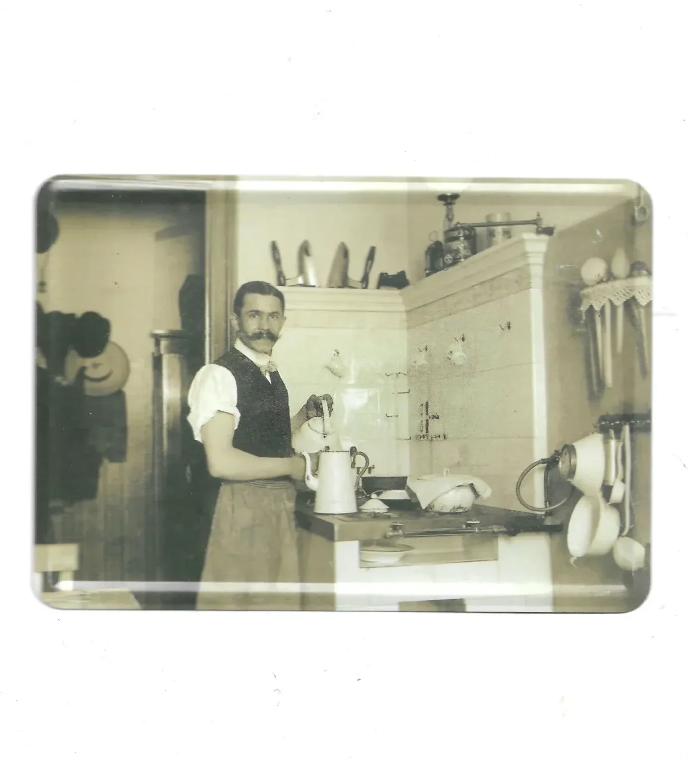 „Blechpostkarte mit Schwarz-Weiß-Foto: Mann in historischer Küche mit Töpfen, Schürze und Kochgeschirr, ca. 10 × 14 cm.“