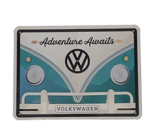 das schild zeigt einen Ausschnitt von der Front eines VW Bulli, Stoßstange, Scheinwerfer, weißer dreiecksausschnitt einmündend in türkisfarbene vW Front Aufschrift: Adventures Awaits Emblem VW beides in schwarz