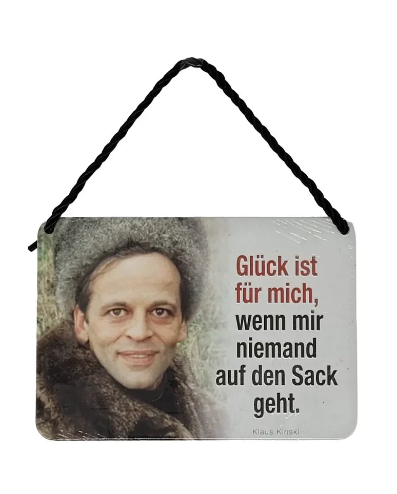 „Hängeschild mit Schwarz-Weiß-Foto von Klaus Kinski in Fellmantel und Mütze, daneben der Spruch: ‚Glück ist für mich, wenn mir niemand auf den Sack geht.‘“