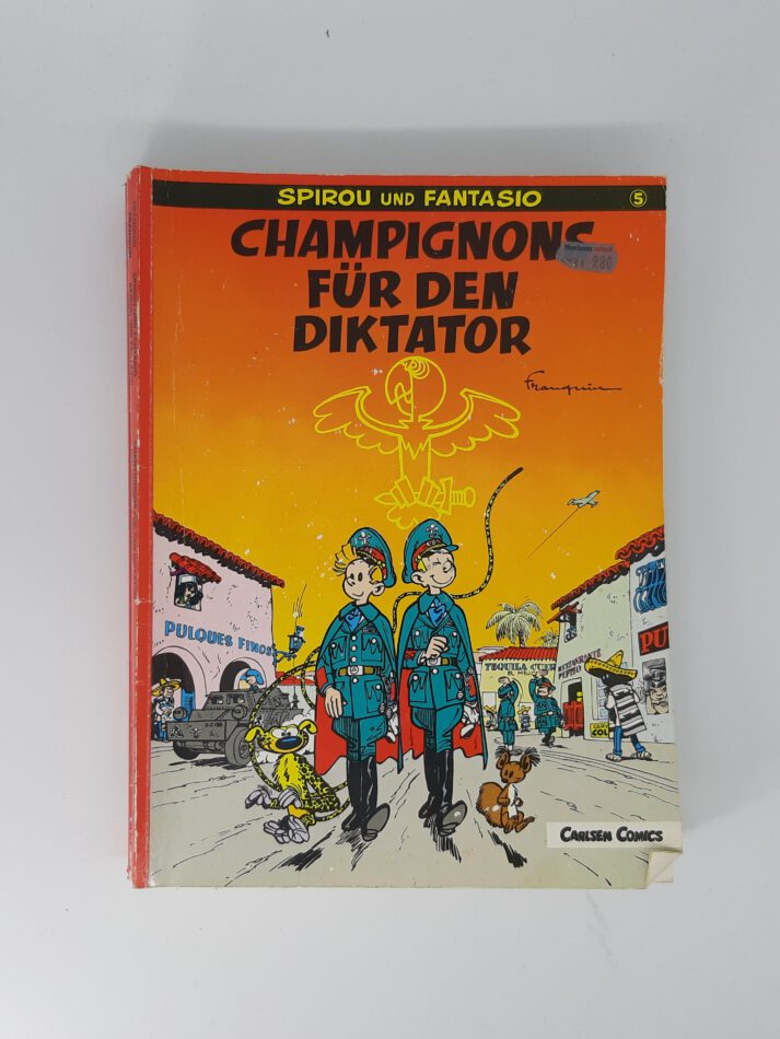 „Comiccover von ‚Spirou und Fantasio – Champignons für den Diktator‘, Carlsen Verlag. Spirou und Fantasio stehen in tropischer Umgebung, das Marsupilami springt im Hintergrund. Titel in roter Schrift, dynamische Szene mit Dschungel und Militärmotiven.“