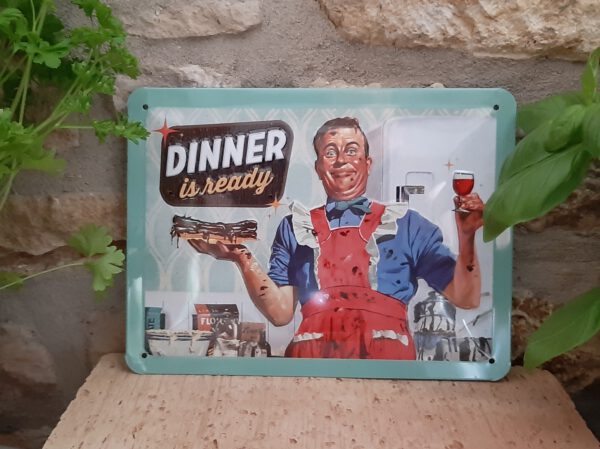 ein Mann, fünfziger Jahre Style blickt stolz drein, Dinner is ready, dabei sind seine Arme, sein Gesicht bekleckert mit Lebensmittelrückständen bzw Schokolade, im Hintergrund eine völlig zugekleckerte Küche