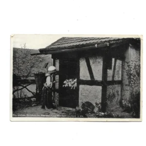 „schwarz-weiß bedruckte Ansichtskarte aus den 1960er Jahren mit Märchenszene aus dem Märchenhain Niederheimbach am Rhein. Motiv zeigt Figuren aus der Wolf und die sieben die sieben Geisslein - Abschied der Mutter und zeigt ein Haeusschen mit dekorativen Elementen.“