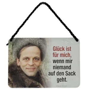 „Hängeschild mit Schwarz-Weiß-Foto von Klaus Kinski in Fellmantel und Mütze, daneben der Spruch: ‚Glück ist für mich, wenn mir niemand auf den Sack geht.‘“