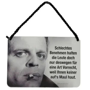 „Blechpostkarte mit Schwarz-Weiß-Foto von Klaus Kinski, Zigarette im Mund, Zitat rechts: ‚Schlechtes Benehmen halten die Leute doch nur deswegen für eine Art Vorrecht, weil Ihnen keiner auf’s Maul haut.‘“